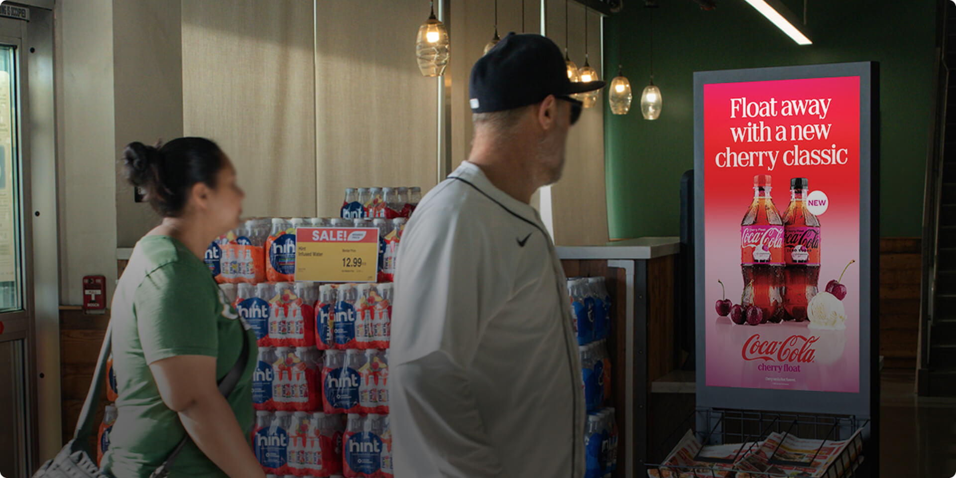 Image of shoppers targeted based on geographic, demographic, and/or behavioral features looking at a digital screen placed at the entrance of a grocery store